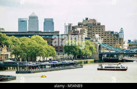 A river boat is seen leaving the dock next to Tower Bridge with Canary Wharf in the backgroun in London Stock Photo