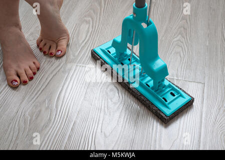 Female feet and blue mop on laminate background Stock Photo