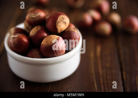 Hazelnuts in white ceramic bowl on wooden background. Monochrome. Macro. With shells. Stock Photo