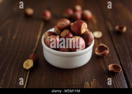 Hazelnuts in white ceramic bowl on wooden background. Monochrome. Macro. With shells. Stock Photo