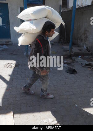 Gaza, Palestinian Territories. 13th Feb, 2018. A young man carries flour sacks to an aliment distribution centre of UNRWA in Gaza, Palestinian Territories, 13 February 2018. His clothes are covered in white because of the flour. UNRWA distributes basic aliments to approximately one million people in Gaza. Credit: Stefanie Järkel/dpa/Alamy Live News Stock Photo