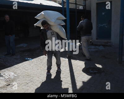 Gaza, Palestinian Territories. 13th Feb, 2018. A young man carries flour sacks to an aliment distribution centre of UNRWA in Gaza, Palestinian Territories, 13 February 2018. His clothes are covered in white because of the flour. UNRWA distributes basic aliments to approximately one million people in Gaza. Credit: Stefanie Järkel/dpa/Alamy Live News Stock Photo