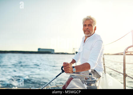 Mature man sitting alone on the deck of his yacht sailing on the open ocean on a sunny afternoon Stock Photo