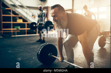 Mature man with a beard wearing sportswear preparing to lift weights while working out in a gym Stock Photo
