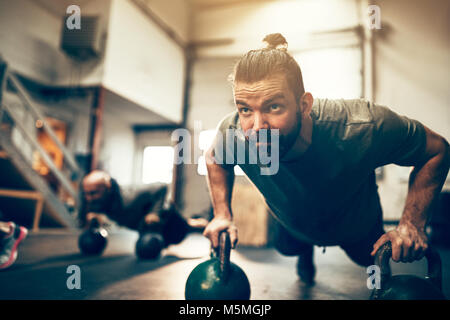 Fit young man doing pushups on dumbbells during an exercise class in a gym Stock Photo
