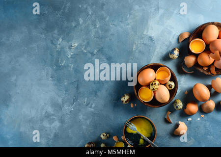 Header with raw brown hen and quail eggs, whole and broken, on two wooden dishes. Concrete background with copy space. Modern Easter concept. Stock Photo