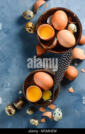 Raw eggs in wooden dishes from above. Cooking with fresh ingredients concept. Brown eggs on a concrete background with feathers close-up. Stock Photo