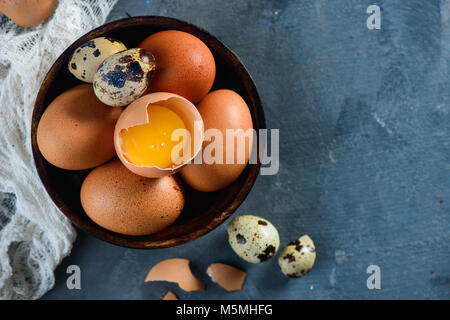 Header with raw brown hen and quail eggs, whole and broken, on a wooden dish. Concrete background with copy space. Modern Easter concept. Stock Photo