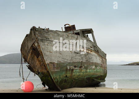 Close up of an old wooden shipwrecked boat run aground on a tan sandy beach on New Island in the Falkland Islands. A hot pink buoy is hanging off the  Stock Photo