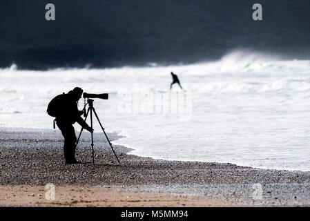 The silhouette of a photographer setting his equipment on the beach at Fistral in Newquay, Cornwall. Stock Photo