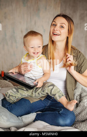 Happy mom and cute child boy laughing having fun and using tablet at home Stock Photo
