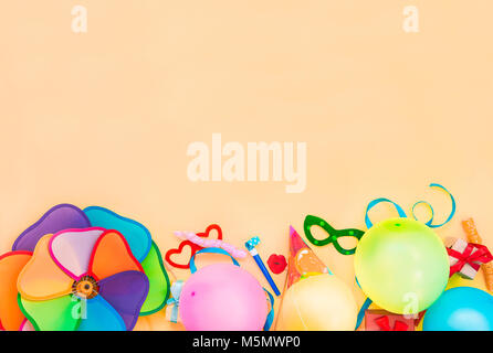 Top view bright party tools and decoration - baloons, funny carnival masks, festive tinsel on peach color background. Happy birthday greeting card. Design concept. Select focus, place for text. Stock Photo