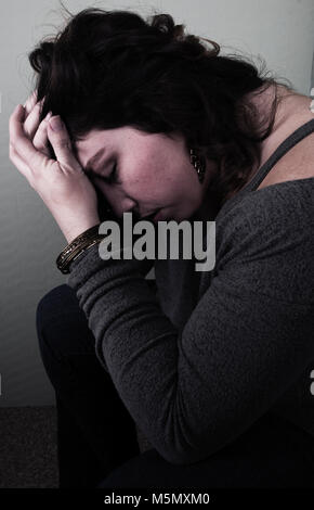 Young woman sitting with her hand to her face looking upset. Stock Photo