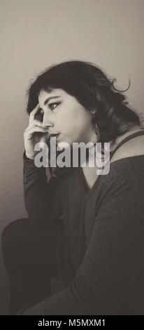 Young woman sitting with her hand to her face looking upset. Stock Photo
