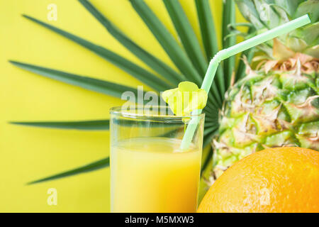 Close up of Tall Glass with Freshly Pressed Pineapple Orange Coconut Juice Straw and Small Flower. Round Palm Tree Leaf on Yellow Background. Vacation Stock Photo