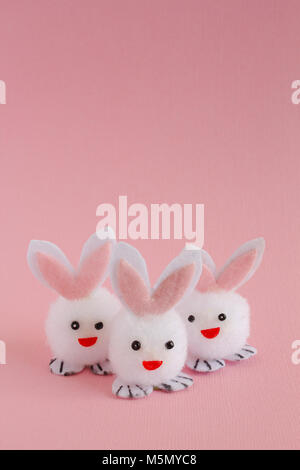 Three fuzzy white pom pom Easter bunnies with pink ears on a pink background. Stock Photo