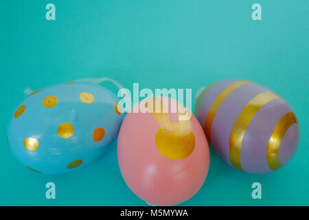 Three painted eggs for Easter. A blue with gold spots, pink with a gold bunny & a purple with gold stripes. Stock Photo