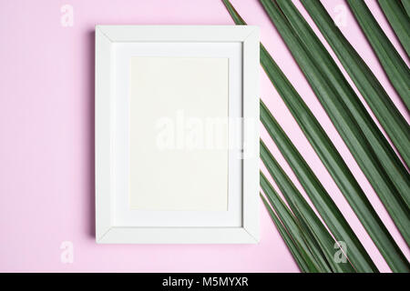 Top view blank white photo frame on green palm leaf on pastel pink table top background.Summer vacation backdrop.Mock up for display design and text Stock Photo