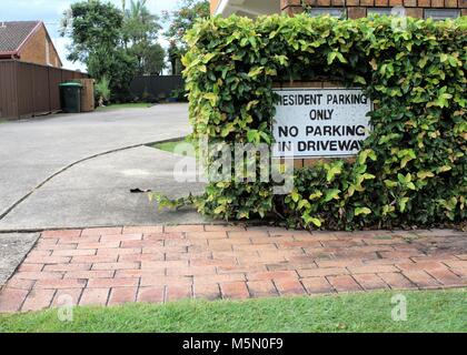 Sign says 'Resident parking only. No parking in driveway.' Sign on wall outside driveway. Stock Photo