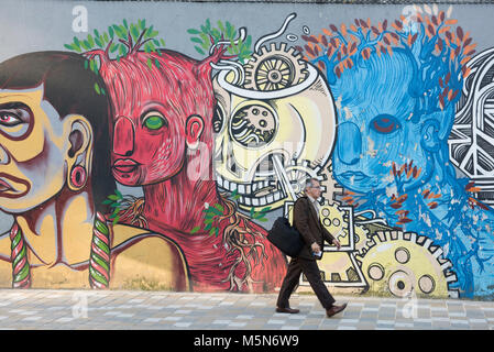 A Colombian man walks past a wall of graffiti. Graffiti decorates many public spaces in Bogota the capital of Colombia Stock Photo