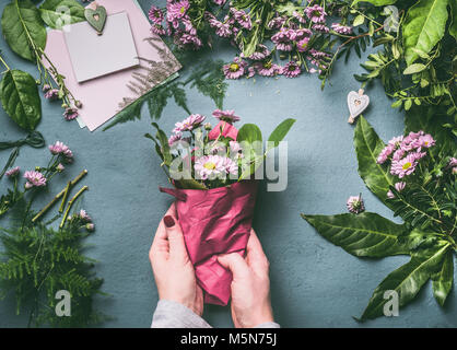 Female hand making beautiful bouquet of pink flowers on florist workspace, top view. Woman wrap bouquet in wrapping paper, step by step Stock Photo