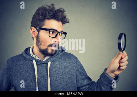 Young scrupulous man looking through magnifying glass in search. Stock Photo