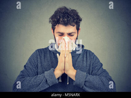 Young man having running nose and blowing it on handkerchief suffering from flu. Stock Photo