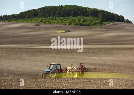 tractor spraying the chemicals on the field. tractor sprinkling pesticides against bugs on agricultural field. Stock Photo