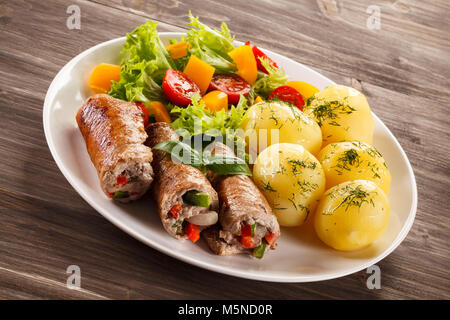 Wrapped pork chop, boiled potatoes and vegetables on wooden background Stock Photo