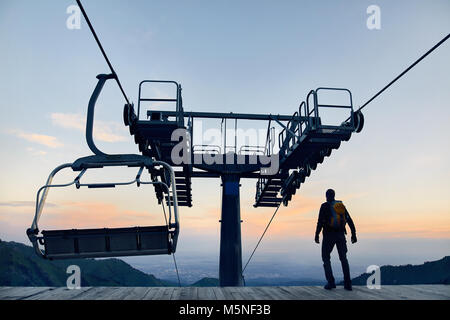 Tourist man walking at ski lift station in silhouette high in mountain ski resort at sunrise