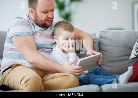 Image of father with son with tablet sitting on gray sofa at home Stock Photo