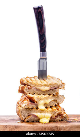 Stack of freshly cooked cheese and ham toasted sandwiches on a wooden serving board with a knife over a white background Stock Photo