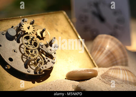 Abstract background with old clock mechanism standing on sand with stones and shells Stock Photo