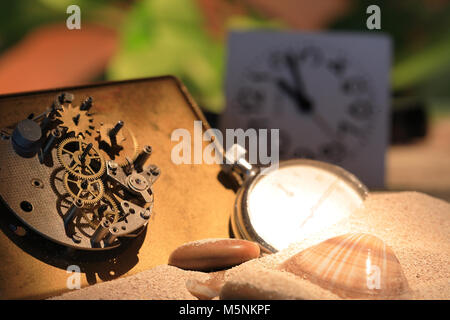 Abstract background with old clock mechanism standing on sand with stones and shells Stock Photo