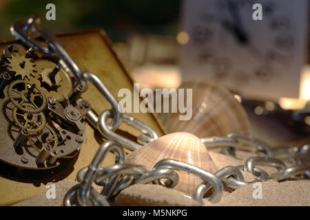 Abstract background with old clock mechanism standing on sand with stones and shells and chain Stock Photo