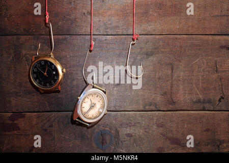 Two old watches hanging on fish hooks on wooden background Stock Photo