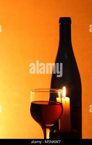 Wineglass near bottle of red wine and candle on nice red background Stock Photo