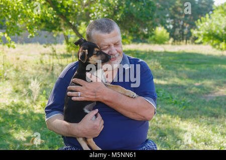 Outdoor portrait of senior man with black little puppy on the hands Stock Photo