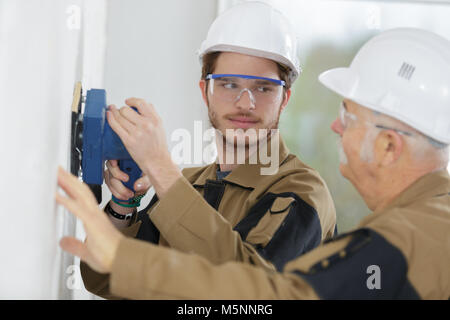 young builder apprentice in hardhat sanding wall indoors Stock Photo