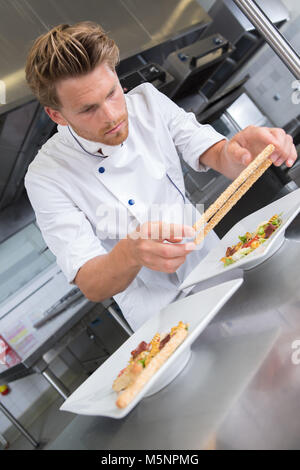 chef sprinkling spices on dish in commercial kitchen Stock Photo
