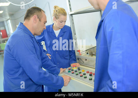 Man explaining controls of machinery to two apprentices Stock Photo