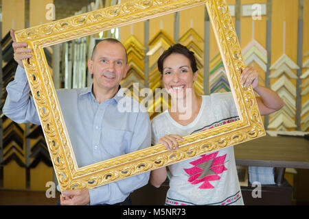 Middle aged man and woman looking through empty picture frame Stock Photo