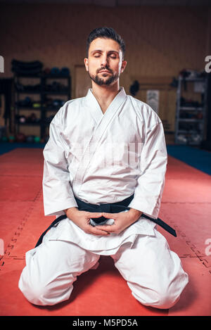 Martial arts, man in white kimono with black belt, meditating in gym Stock Photo