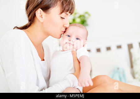 Affectionate mother tenderly kisses her forehead from her infant at home Stock Photo