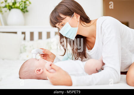 Nurse measures fever in sick baby with forehead thermometer Stock Photo