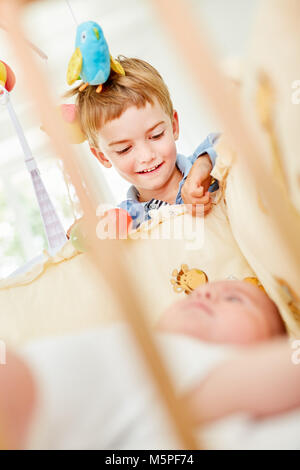 Newborn baby in the cot and smiling boy as a caring brother Stock Photo