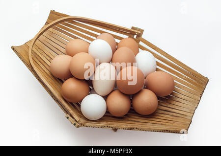 Chicken eggs in a basket of different colors shades on a white background Stock Photo