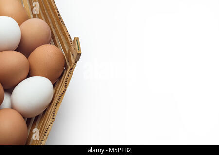 Chicken eggs in a basket of different colors shades close-up on the left edge on a white background Stock Photo