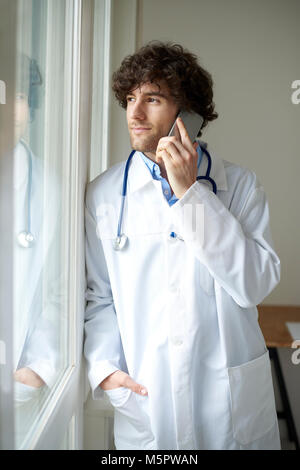 Cropped shot of a young male doctor using mobile phone while talking with his patient. Stock Photo