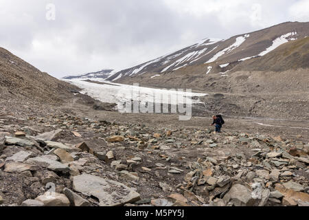 Man searching for fossils in a rocky Longyear glacier moraine in Svalbard, Norway. The glacier edge in the background. Stock Photo